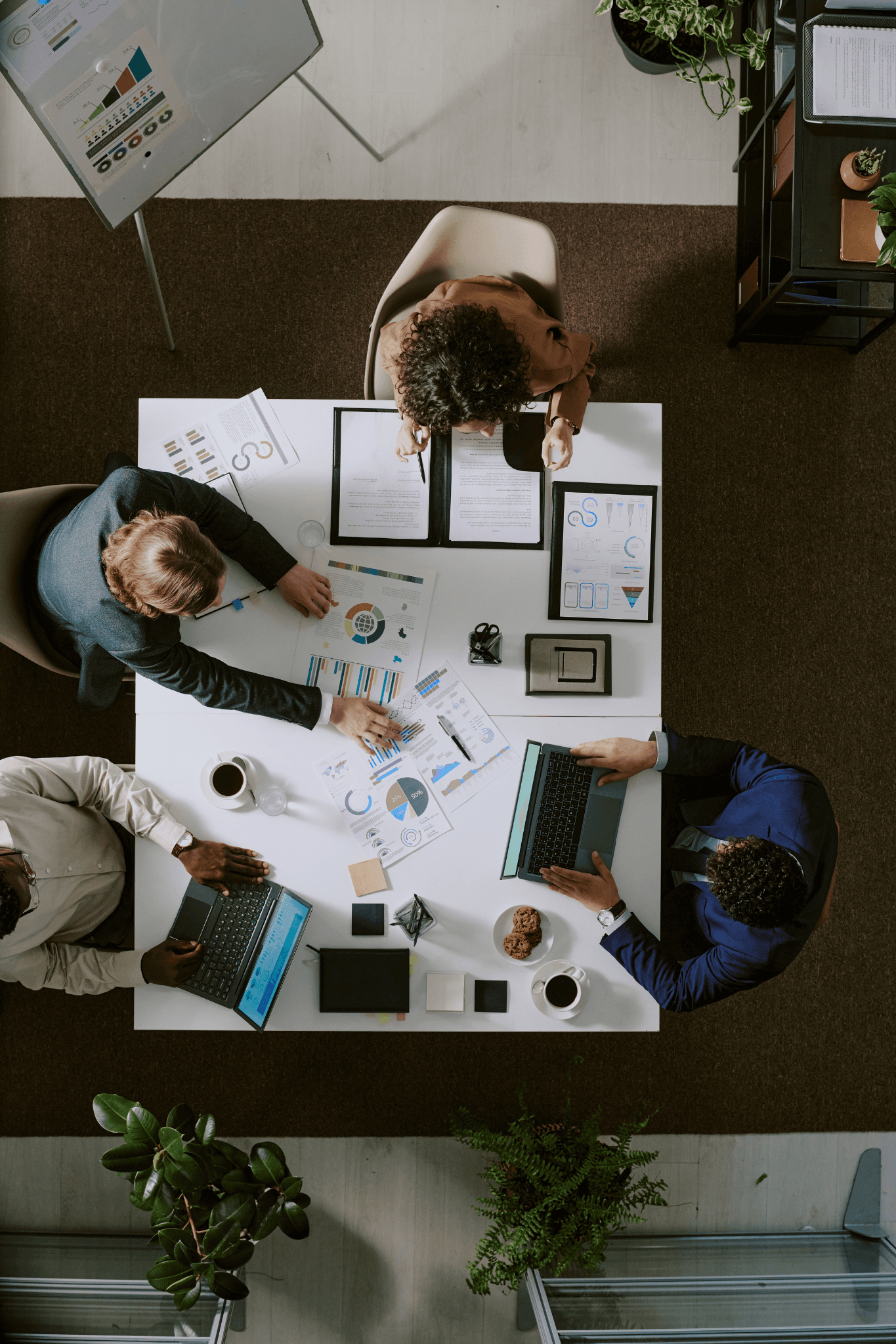 Blick von oben auf vier Personen, die an einem Tisch mit Diagrammen und Laptops zusammenarbeiten