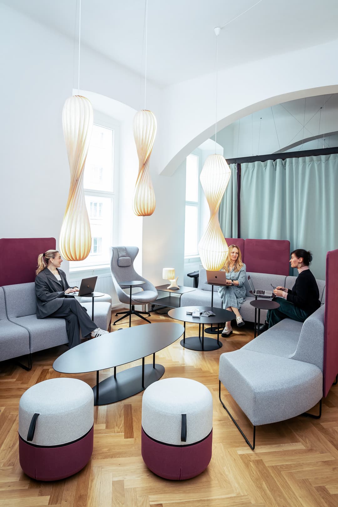 Drei Frauen arbeiten an Laptops in einer hellen Lounge mit Designleuchten und Altbau-Parkett